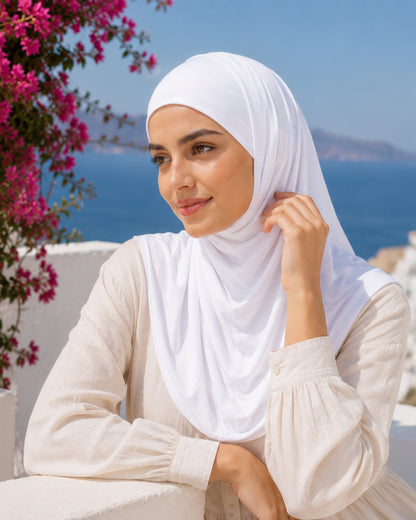 Woman modeling the Layal White two-piece Lycra hijab beside vibrant bougainvillea overlooking the sea, highlighting the hijab's soft drape, comfortable fit, and elegant everyday style.