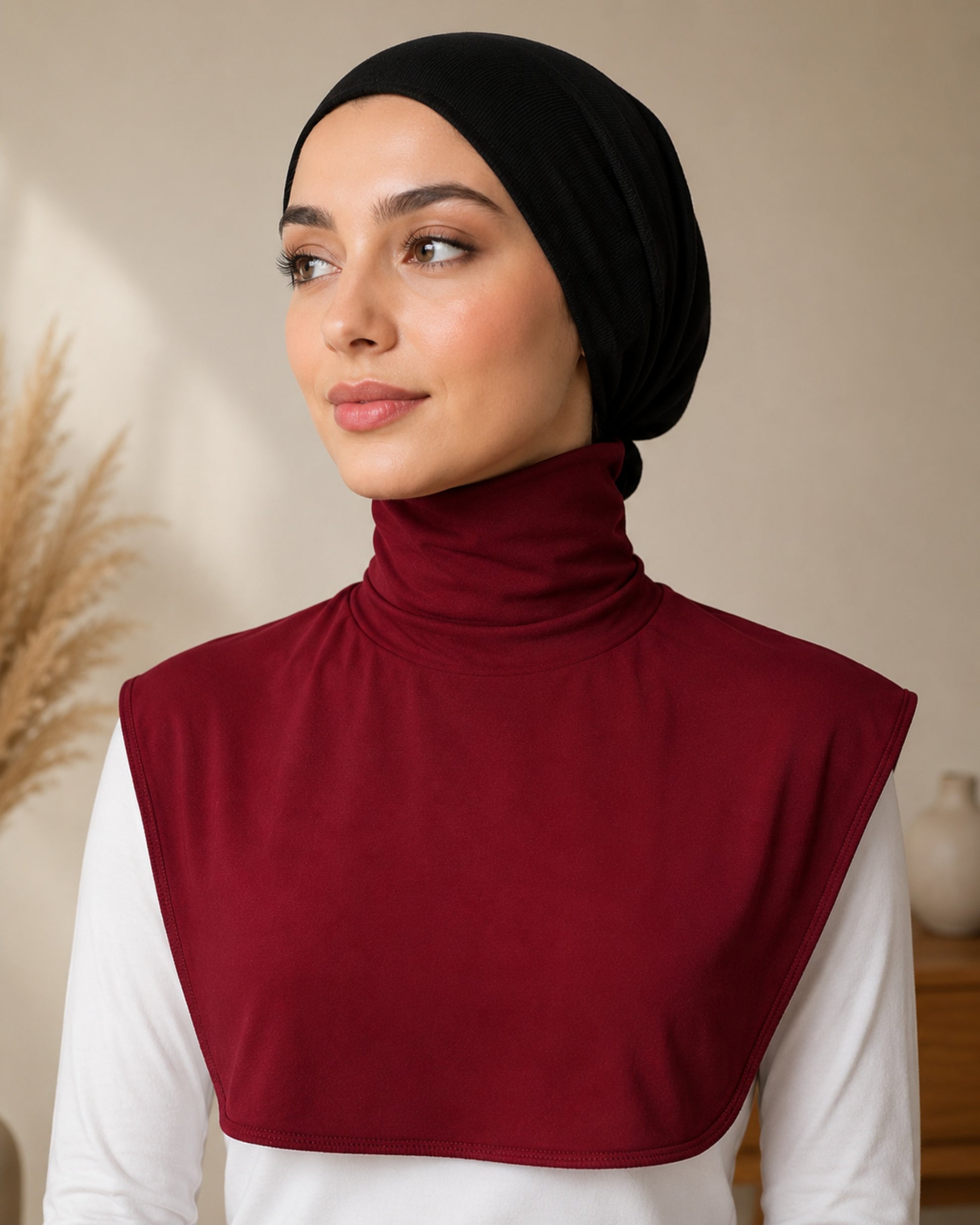 Woman wearing a black hijab and maroon neck cover against a neutral background

