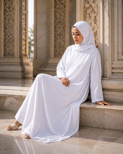 Woman in a white abaya sitting on stone steps with intricate carvings.