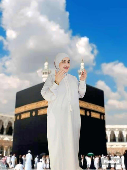 Woman in white hijab standing in front of the Kaaba with a clear blue sky.
